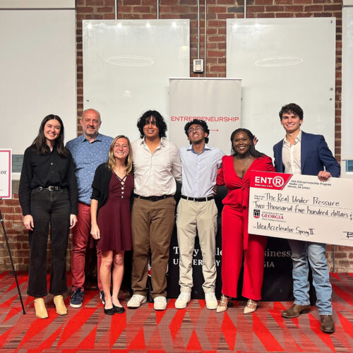 Judges and finalists at the 2024 Spring Idea Accelerator Demo Day gather on the Studio 225 Pitch Deck with the winner holding a large novelty check.