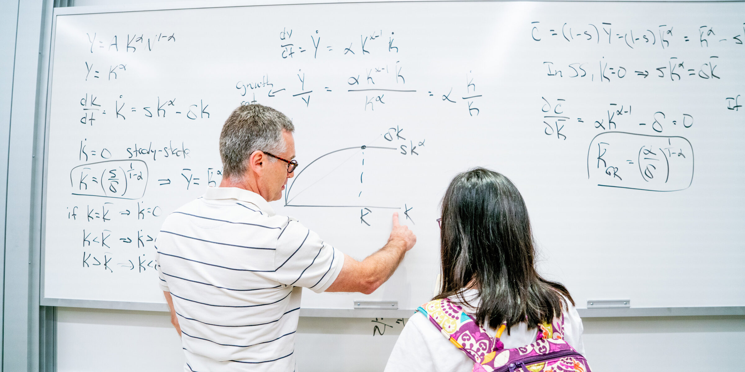 Professor explaining formulas on a white board