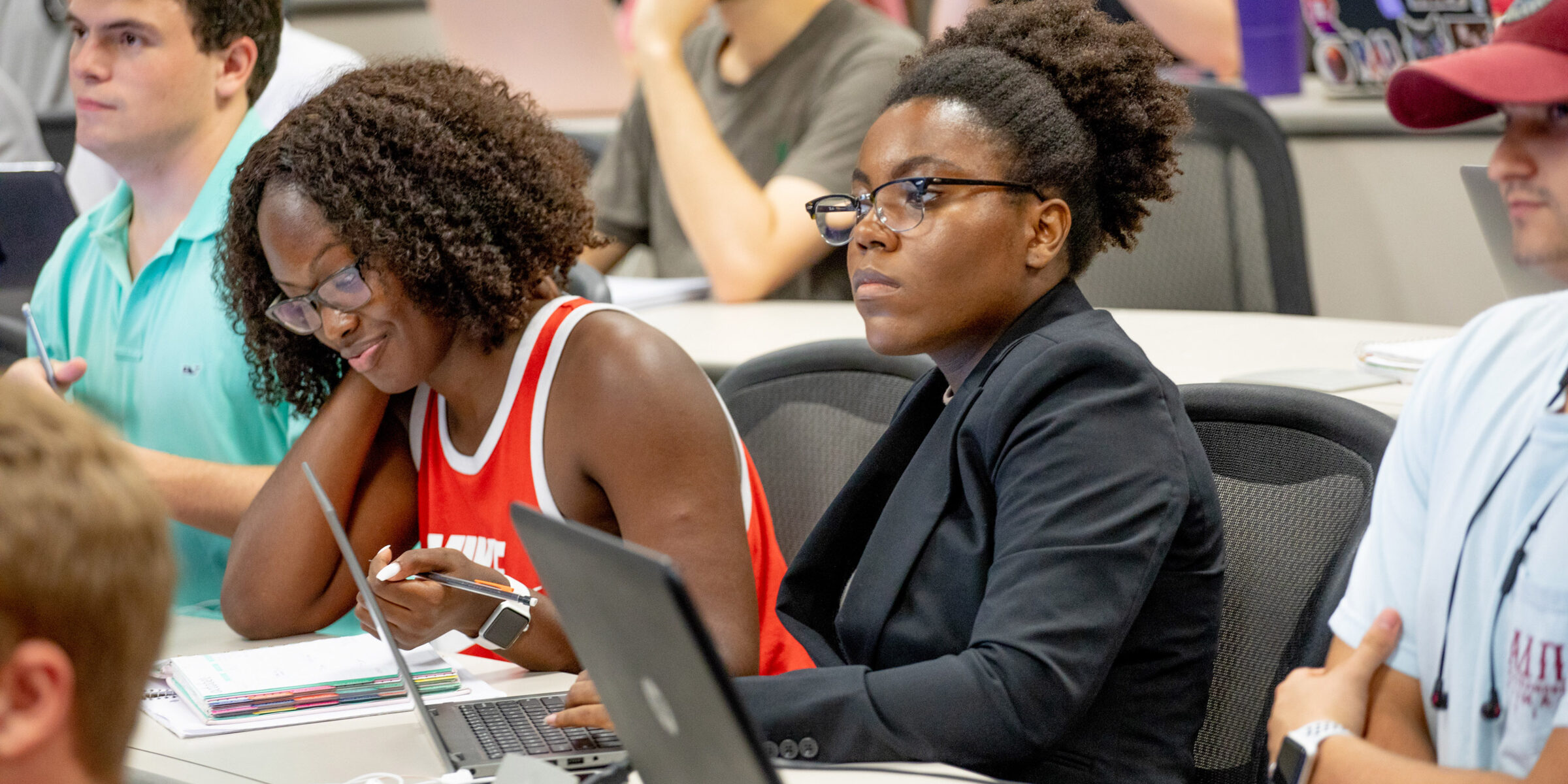 Two black women listening to a lecture in class with other students in the background