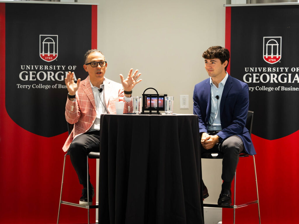 MBA alumnus Paul Donkar talks with Tyler Parks in front of Terry College of business banners at the front Steling stuy