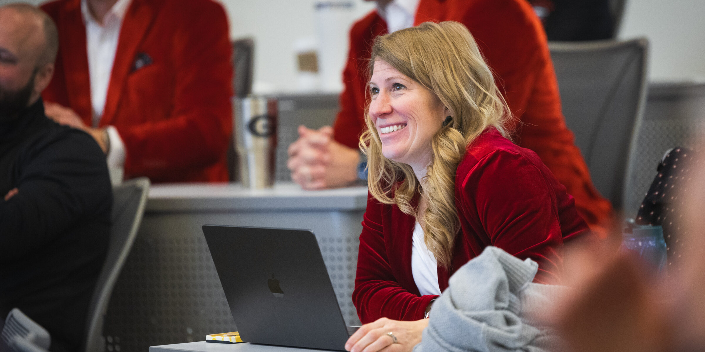 Woman in class at a desk with a laptop in front of her smiling at someone off-screen