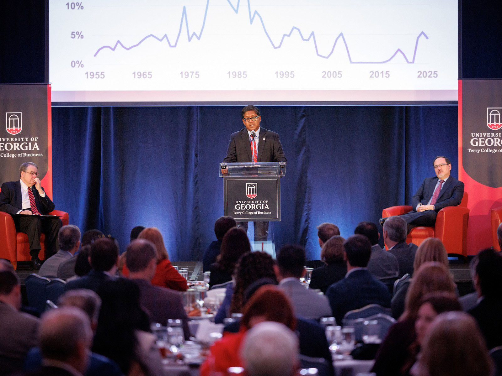 Terry College Interim Dean Santanu Chatterjee delivers the state economic forecast at the UGA's 2026 Economic Outlook in front of large screen showing an economic graph.