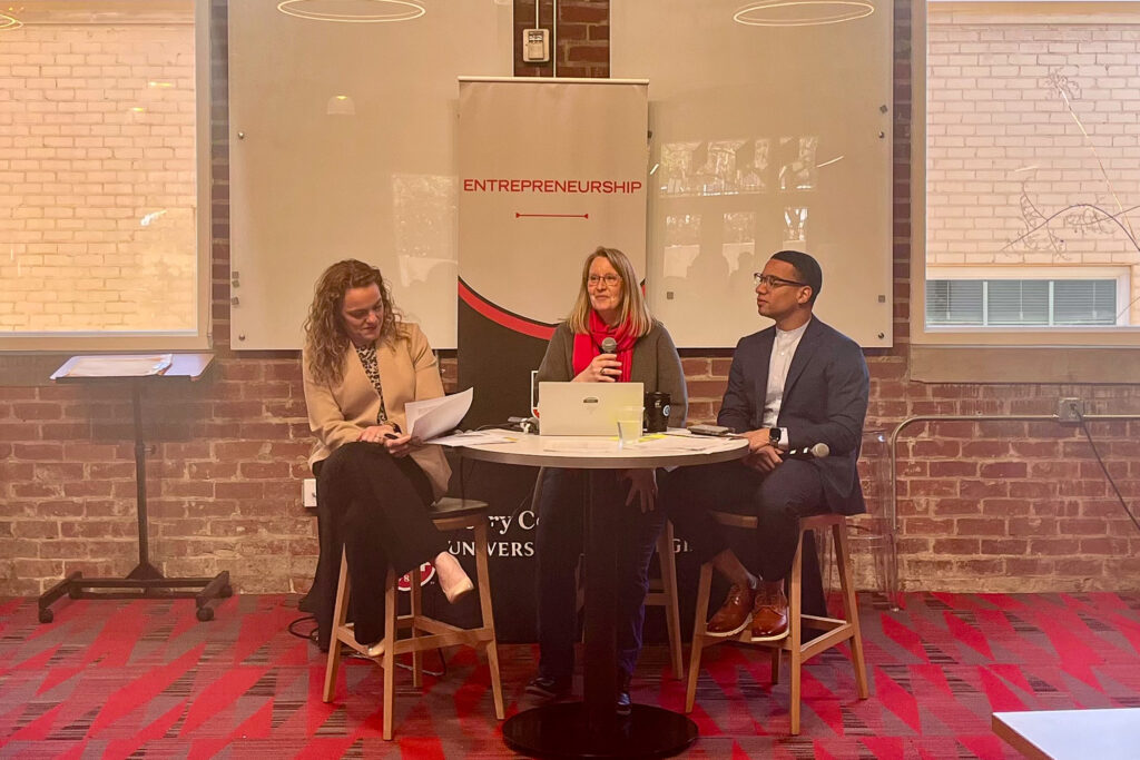 Margaret Price, of UGA, and Jennifer Price and Terrance Griffin, of EY, sit a table holding microphones at the front of a crowd at UGA Studio 225