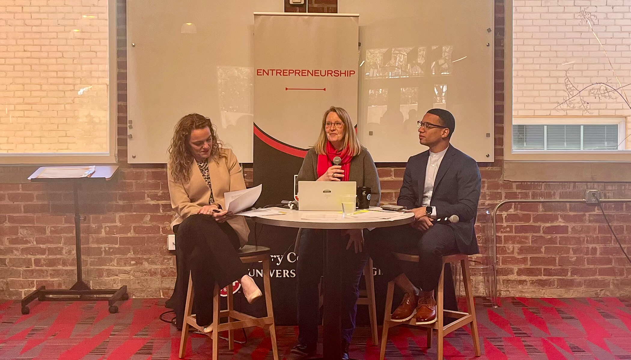 Margaret Price, of UGA, and Jennifer Price and Terrance Griffin, of EY, sit a table holding microphones at the front of a crowd at UGA Studio 225