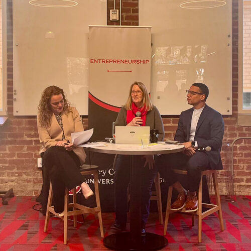 Margaret Price, of UGA, and Jennifer Price and Terrance Griffin, of EY, sit a table holding microphones at the front of a crowd at UGA Studio 225