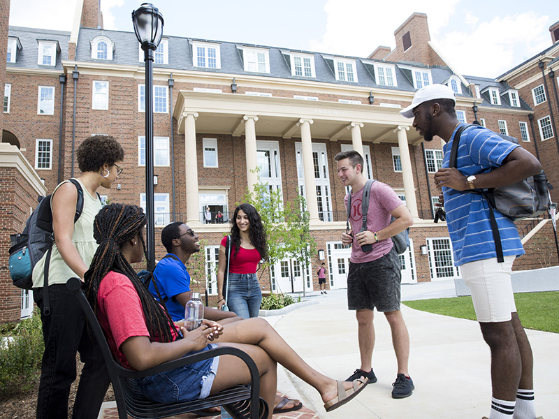 A diverse group of students talking with the Business Learning Community in the background