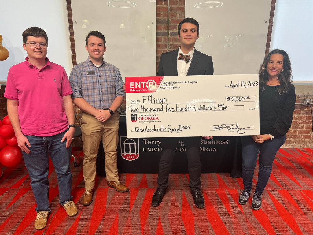 Caleb King holds a novelty prize check with Idea Accelerator judges Trent Walls