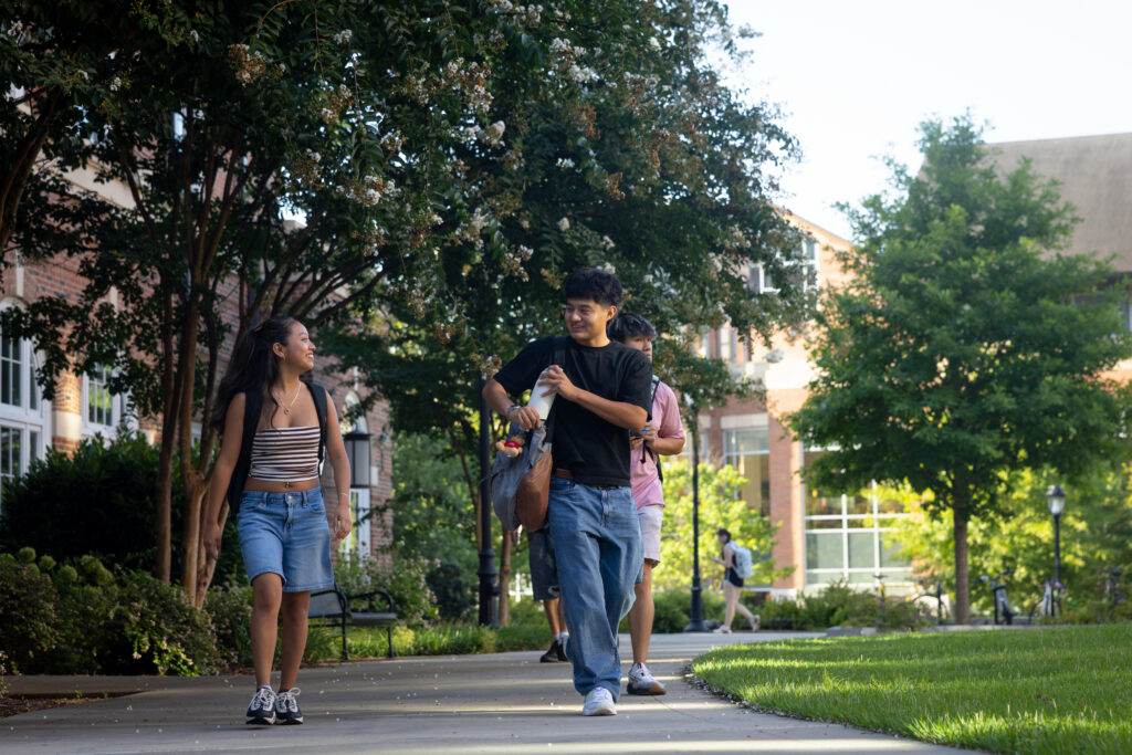 University of Georgia fall semester begins 5 Three young people walk along a tree-lined campus pathway, engaged in conversation as they stroll past brick buildings and greenery. University of Georgia fall semester begins