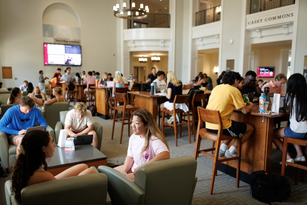 First day Gallery 8 Students study and socialize in a bright, spacious university commons area with high ceilings and wooden tables.