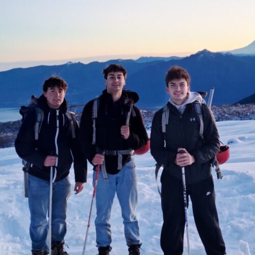 Dylan Foley and 2 other student standing on snowy ground with mountains and a sunset in the background.