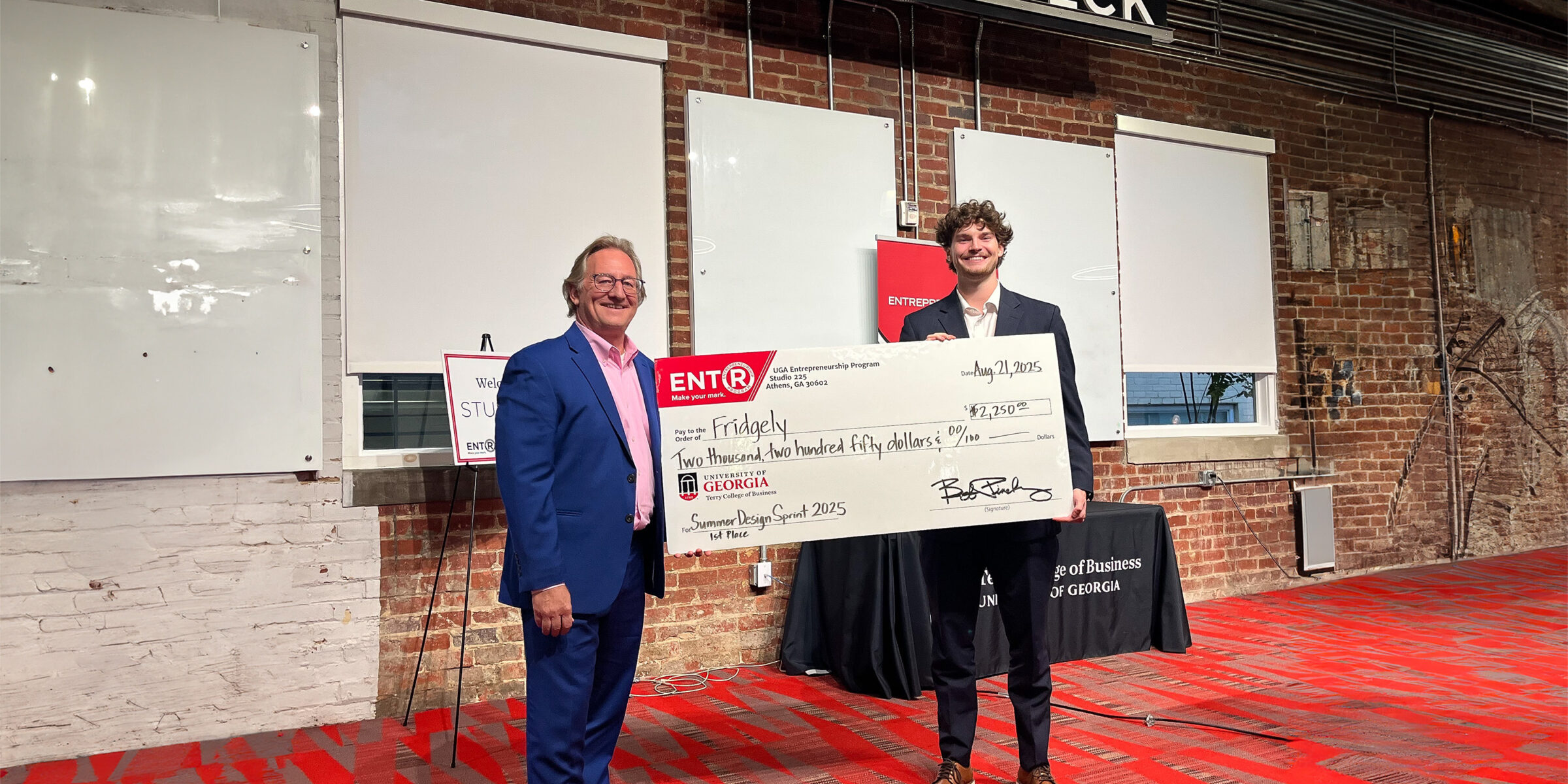 Fridgely wins UGAs 2025 Summer Design Sprint. Design Sprint instructor Don Chambers presents a giant prize check to economics student Gavin Gillespie