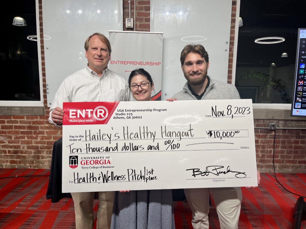 GA Bob Pinckney, director of the UGA Entrepreneurship Program, presents a $10,000 prize check to Hailey Garfinkel (BSFCS '21, MSW '23) and UGA communications student Tyler Lewis after awarding Hailey's Healthy Hangout first prize the UGA Entrepreneurship Program's inaugural Health and Wellness Pitch Competition.