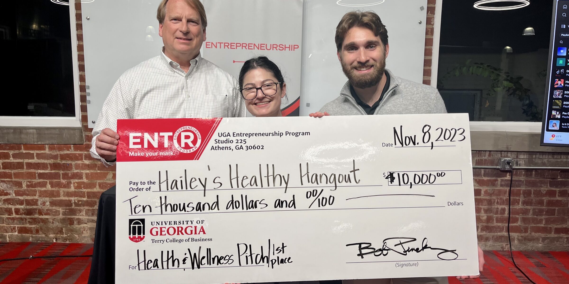 GA Bob Pinckney, director of the UGA Entrepreneurship Program, presents a $10,000 prize check to Hailey Garfinkel (BSFCS '21, MSW '23) and UGA communications student Tyler Lewis after awarding Hailey's Healthy Hangout first prize the UGA Entrepreneurship Program's inaugural Health and Wellness Pitch Competition.