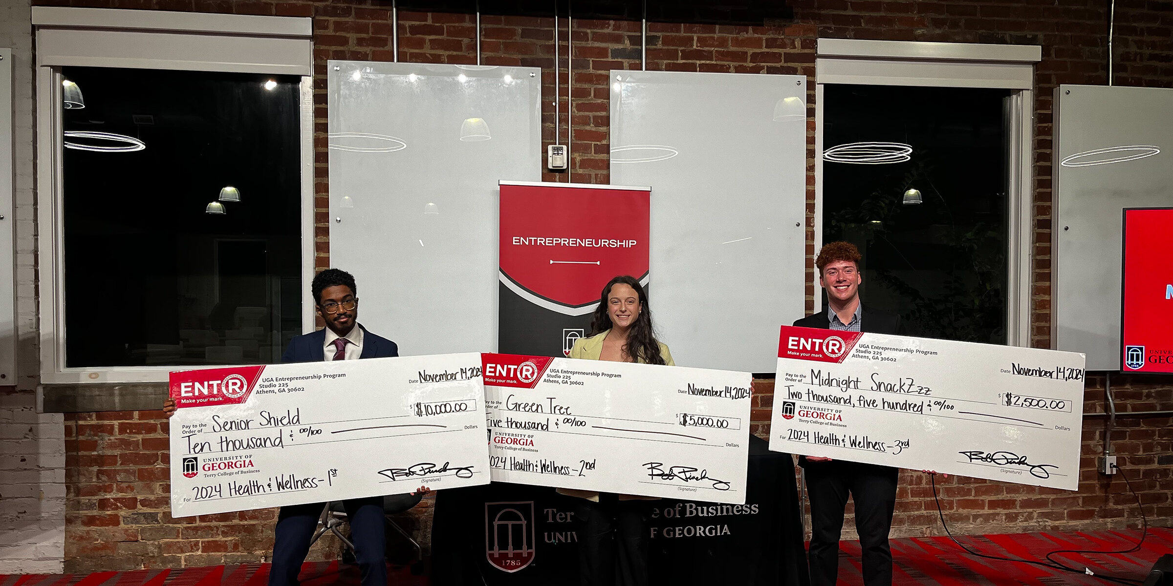 Kareem Elfoulie, Halle Greenbaum and Michael Hearnes stand in front of a sign that says pitch deck at Studio 225.