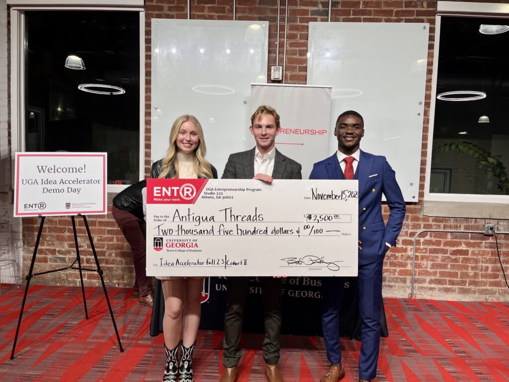 Kelsie Pearson, Moss Davis and Mbeng Juvis pose after pitching at the UGA Idea Acclerator. Davis, in the middle, holds large prize check.