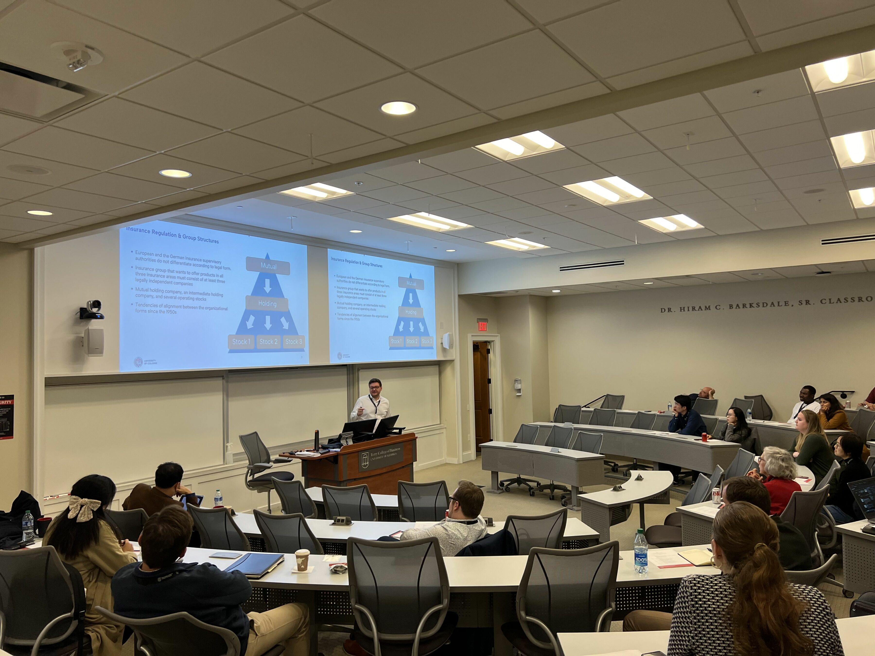 Participants in the Risk Management & Insurance Symposium listen to three speakers sitting in front of them in a BLC classroom.