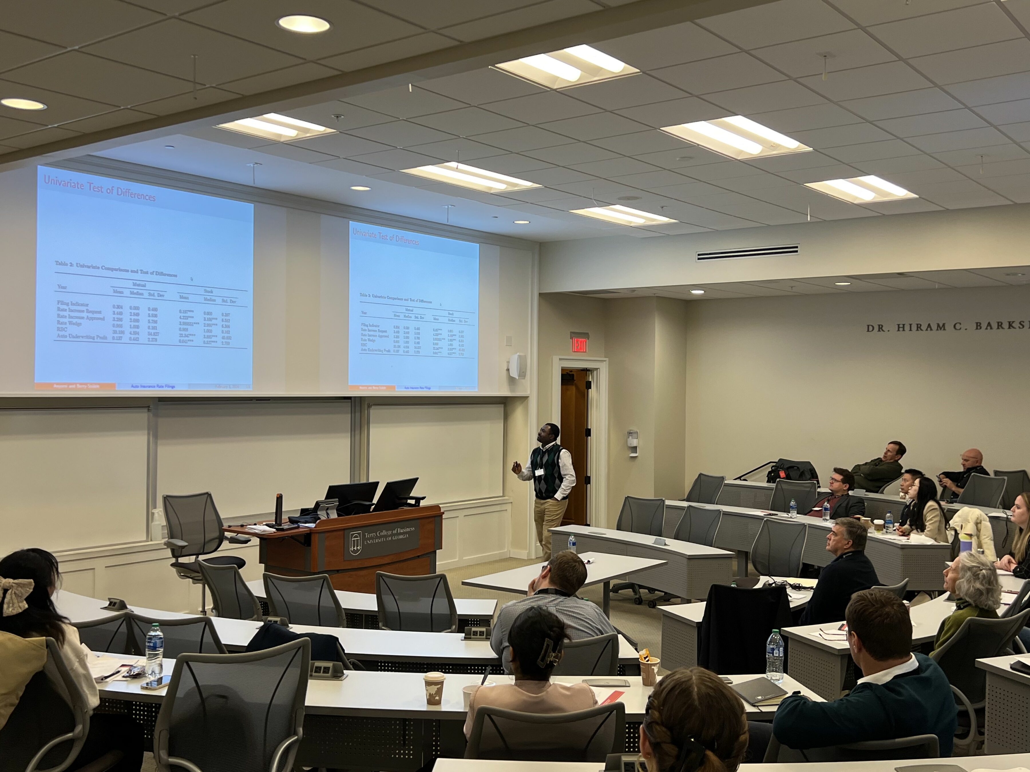 Participants in the Risk Management & Insurance Symposium listen to three speakers sitting in front of them in a BLC classroom.