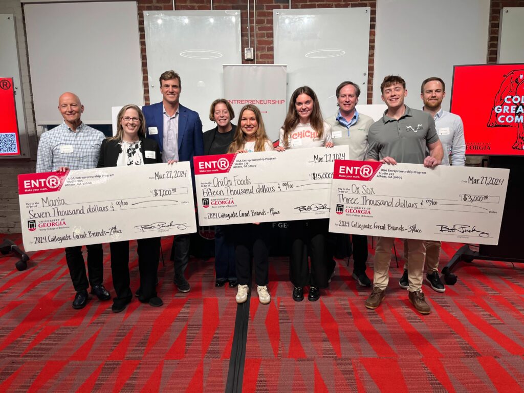 Winners of the 2024 Collegiate Great Brands pitch competition stand with their novelty prize checks with the contest's four judges behind them at Studio 225.