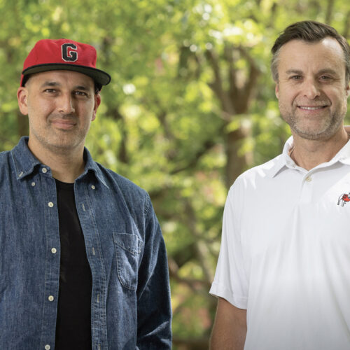 Two men posing in front of greenery