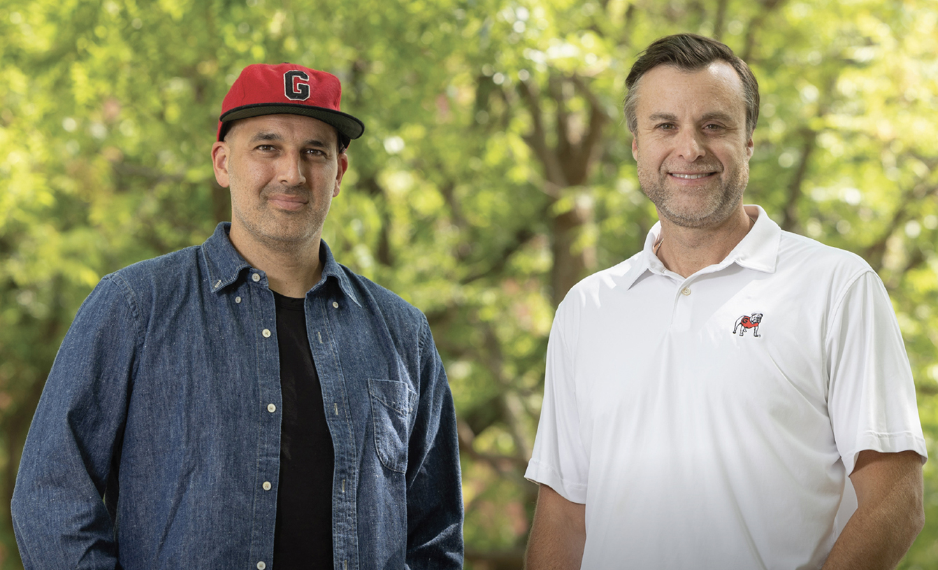 Two men posing in front of greenery