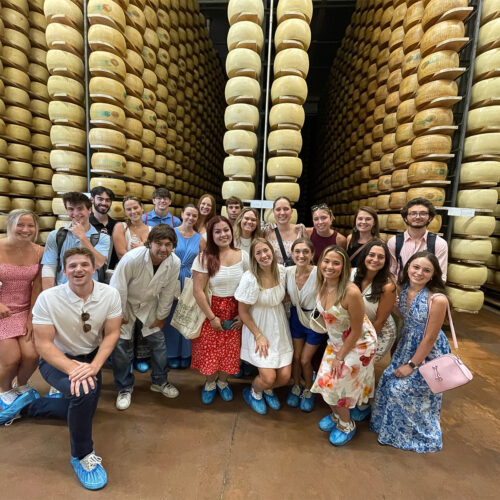 Terry students pose in front of aisles of aging Parmesan cheese at a factory outside of Milan Italy