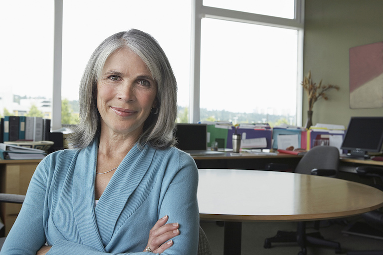 Gray-haired woman standing at table. 