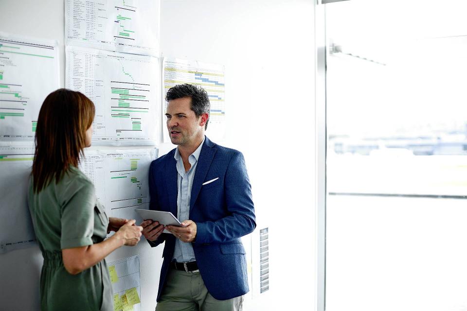 A man talks to a woman in front a dry-erase board in a business setting.