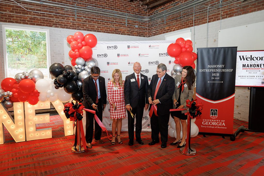 Five individuals participate in a ribbon-cutting ceremony at the University of Georgia's Mahoney Entrepreneurship Hub, surrounded by balloons and event signage.
