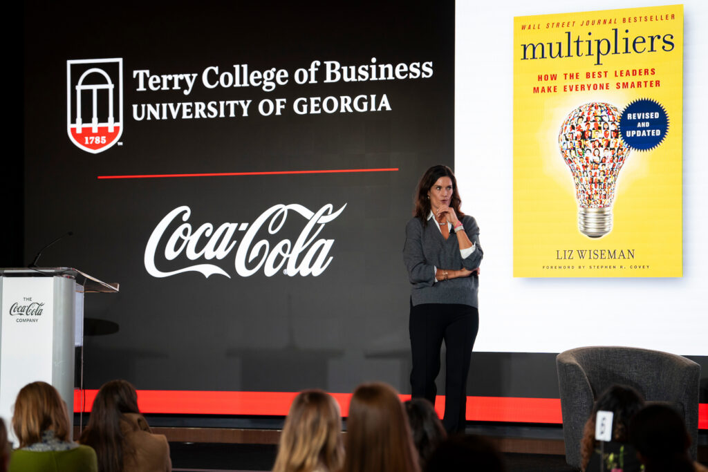 A leadership speaker speaks to the crowd in front of a large slide displaying the cover of the book "Multipliers" at the Terry College Professional Women's Conference.