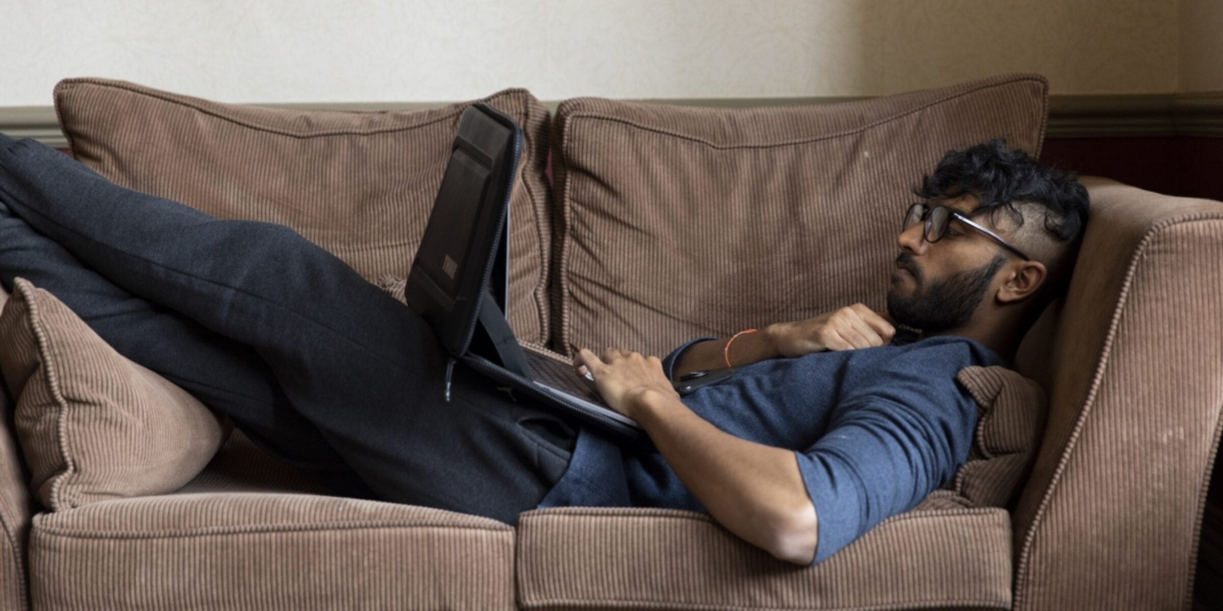 Man lying on couch, working on his laptop.