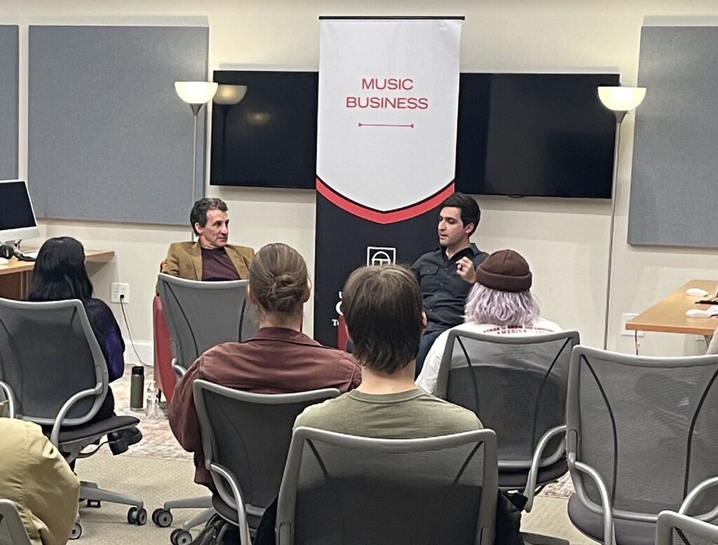 A diverse group of individuals sitting in chairs in a well-lit room, engaged in a discussion or meeting.