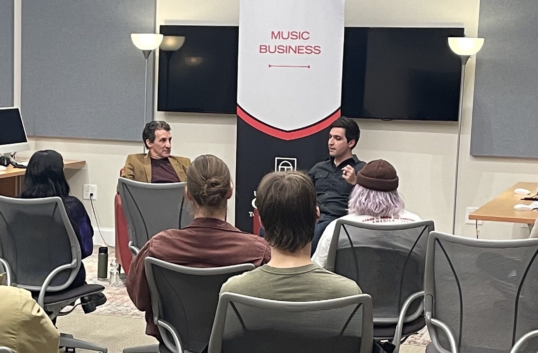 A diverse group of individuals sitting in chairs in a well-lit room, engaged in a discussion or meeting.