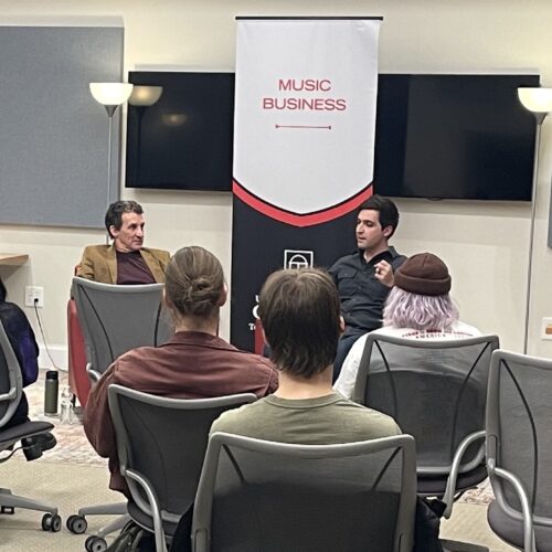A diverse group of individuals sitting in chairs in a well-lit room, engaged in a discussion or meeting.