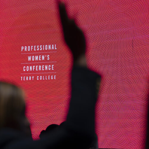 Professional Womens Conference Title Slide with someone raising their hand in front of it .