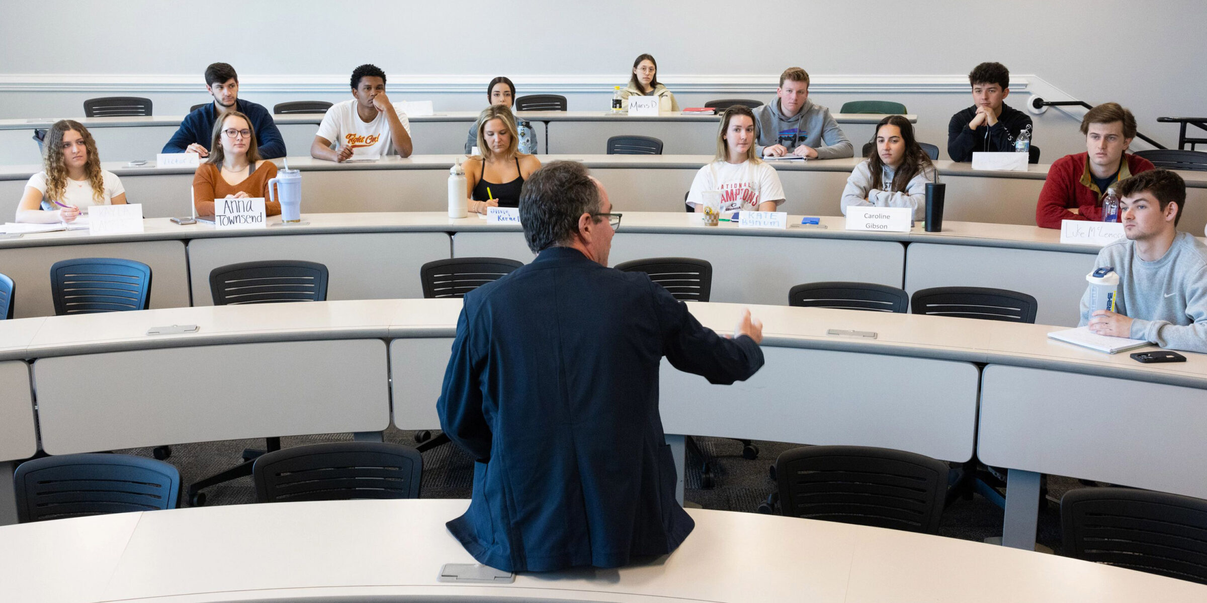 Professor talks with student from the front of a classroom.