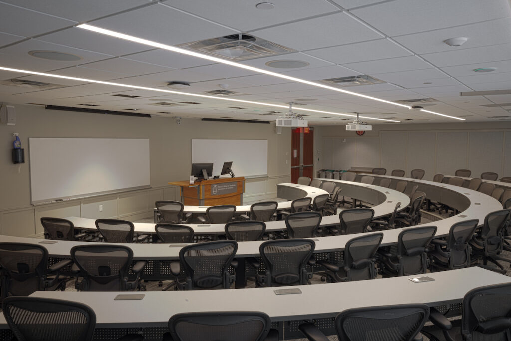 Room365_02 An empty classroom; a podium in the exact center of the room; a 4 rowed semi-circle or tables and chairs is formed around the center; two large white boards on the wall behind the podium.