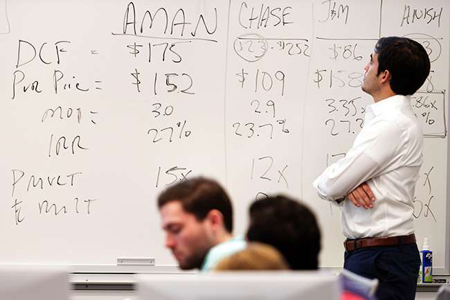 A male student reviews stock market analysis written on a dry erase board.