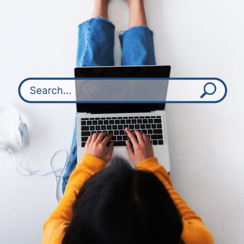 A woman sits on the ground with her laptop using a search engine. A search engine bar is projected into the center of the image.