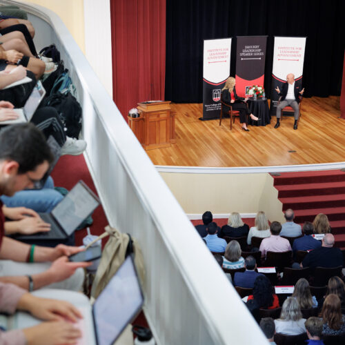 Chick-fil-A CEO Andrew T. Cathy speaing to a ILA student, shot from above on the UGA Chapel stage with students taking notes in the foreground.