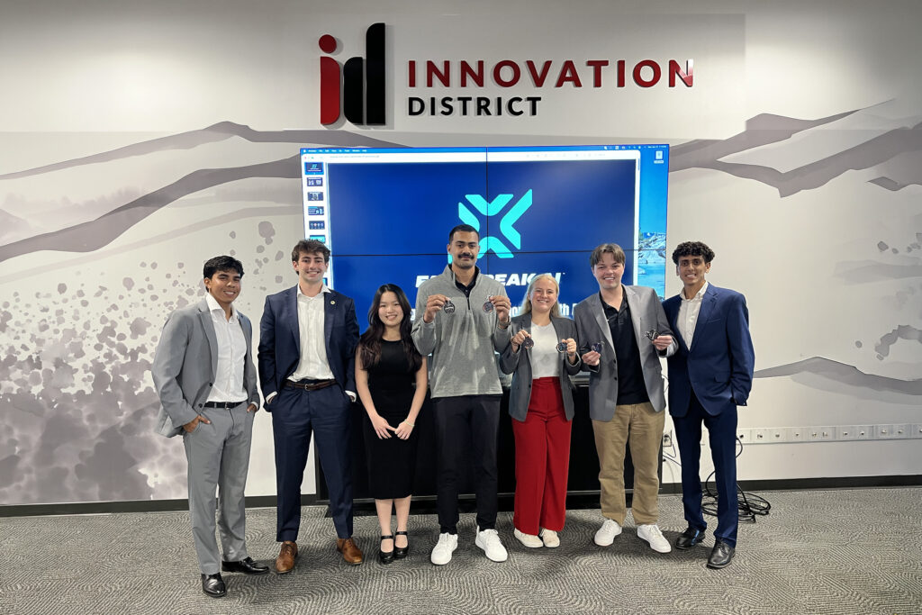 Winners of the 2026 Design Thinking Challenge stand with the general manager of Fastbreak.AI as he holds two "ad tags" a collectible drink top designed for marketers to distribute at sports tournaments.