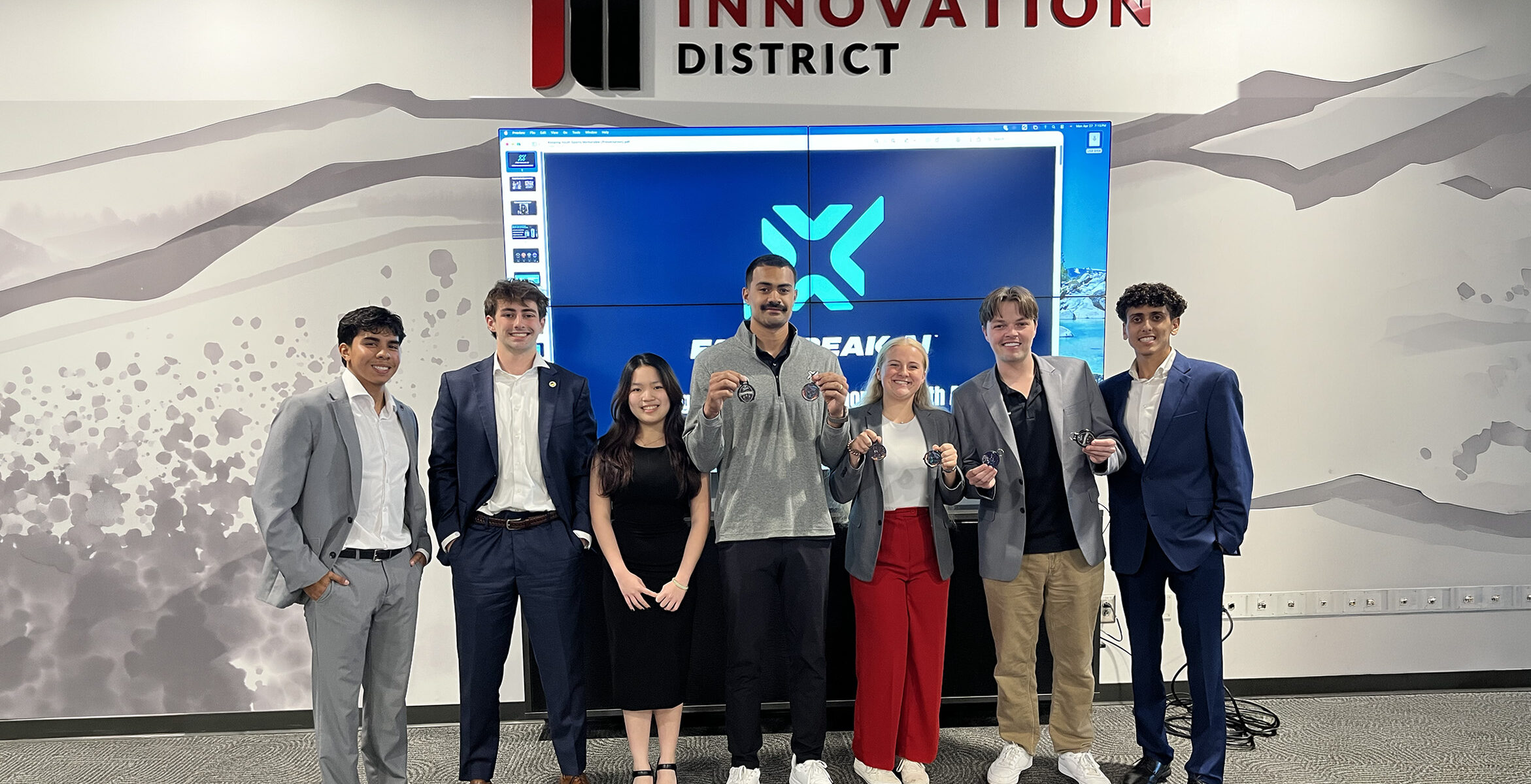 Winners of the 2026 Design Thinking Challenge stand with the general manager of Fastbreak.AI as he holds two "ad tags" a collectible drink top designed for marketers to distribute at sports tournaments.