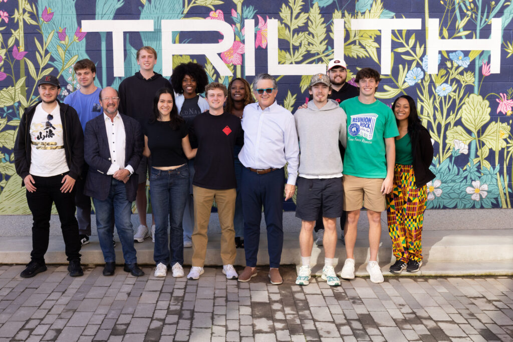 Graduate students stand with Trilith Studios CEO stand in front a floral mural.