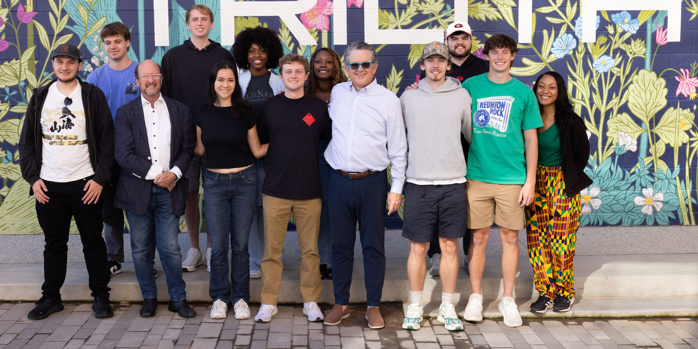 Graduate students stand with Trilith Studios CEO stand in front a floral mural.