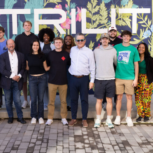 Graduate students stand with Trilith Studios CEO stand in front a floral mural.