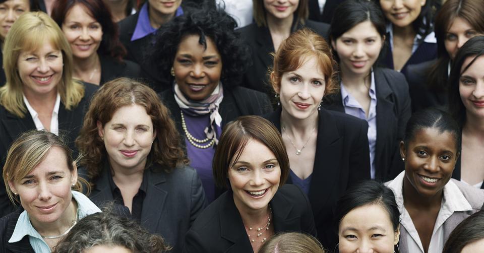 A group of women in business attire look up and smile at the camera.