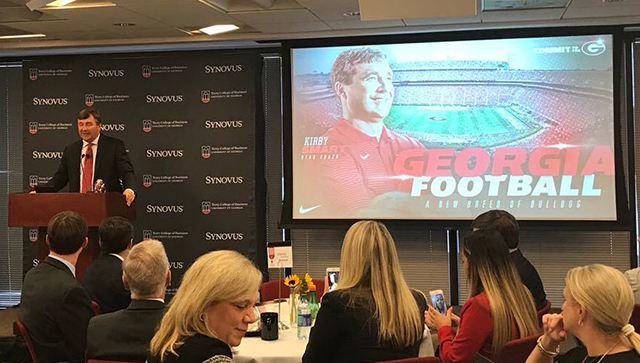 Kirby Smart delivering a presentation in front of a crow of people sitting at round tables