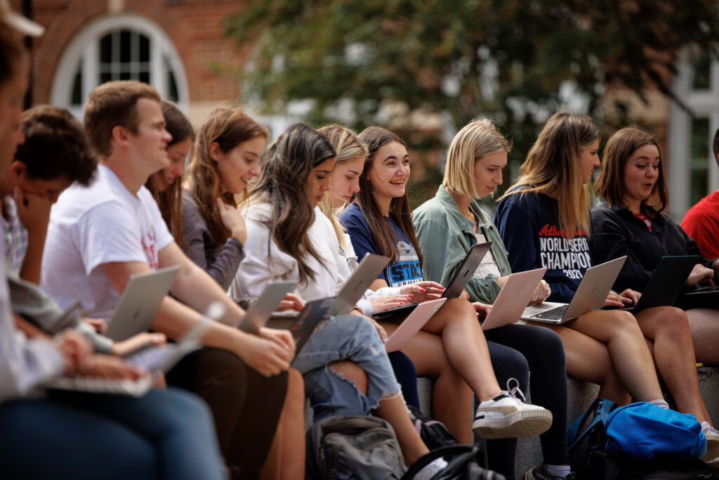 Terry College of Business students sit outside the Business Learning Community with their laptops.