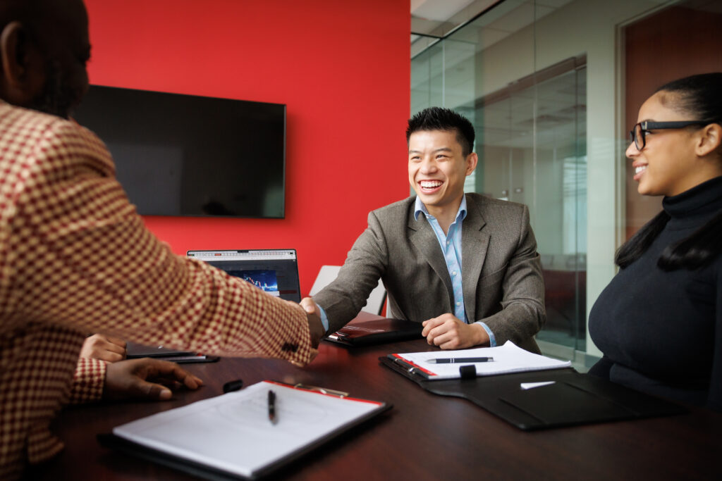 Two men in business attire shake hands at a table,