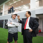 athletic coach chats with man in suit at a football practice facility