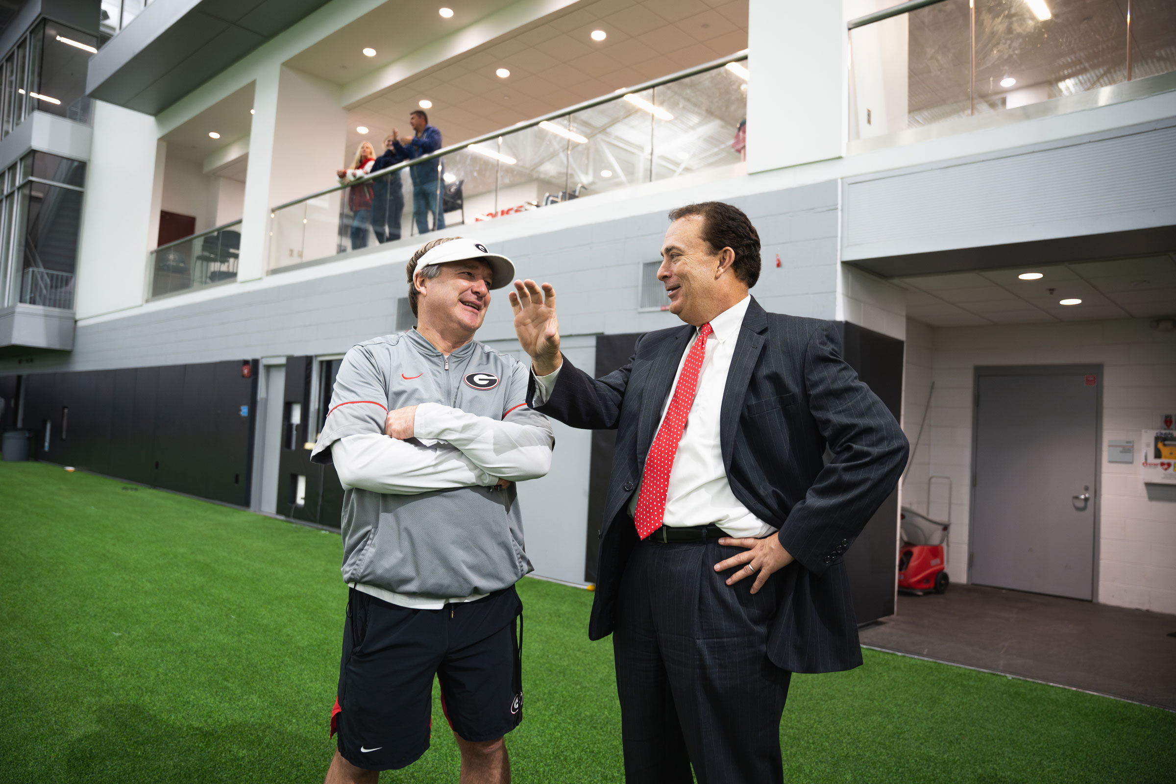 athletic coach chats with man in suit at a football practice facility
